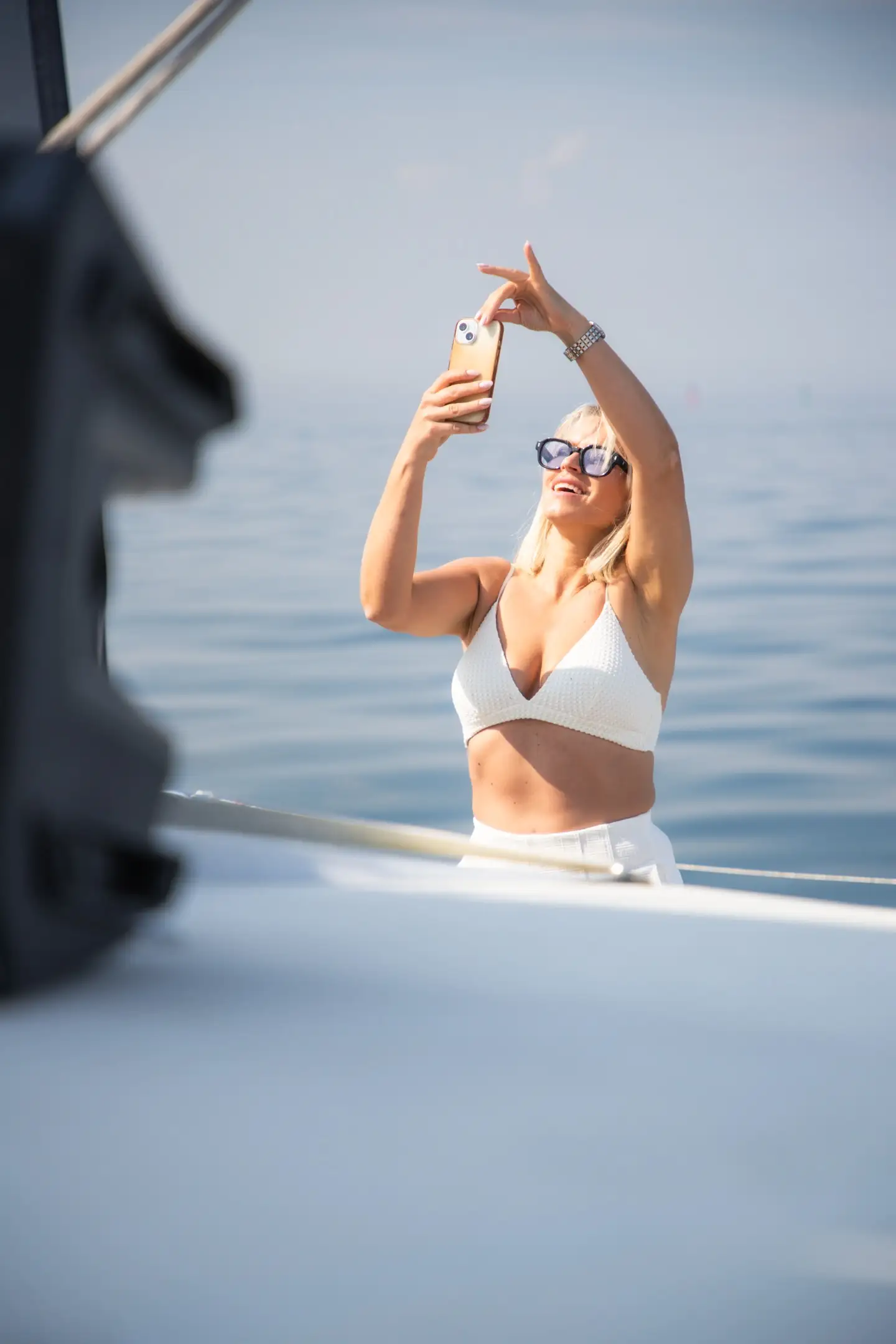 Blondynka w bikini robi selfie na dziobie, spokojne morze w tle, eleganckie światło poranne.